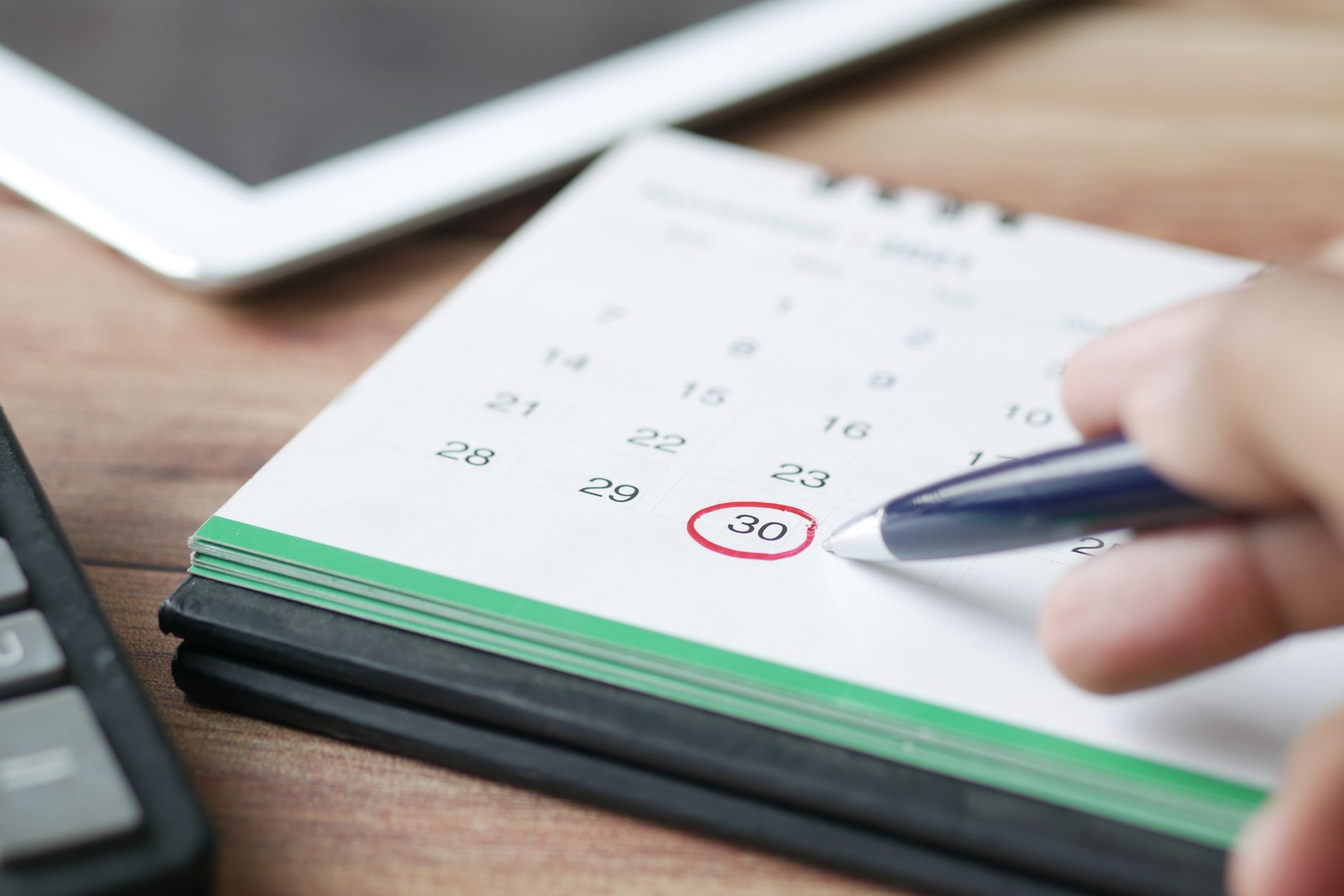 Hand marking a date on a calendar with a pen